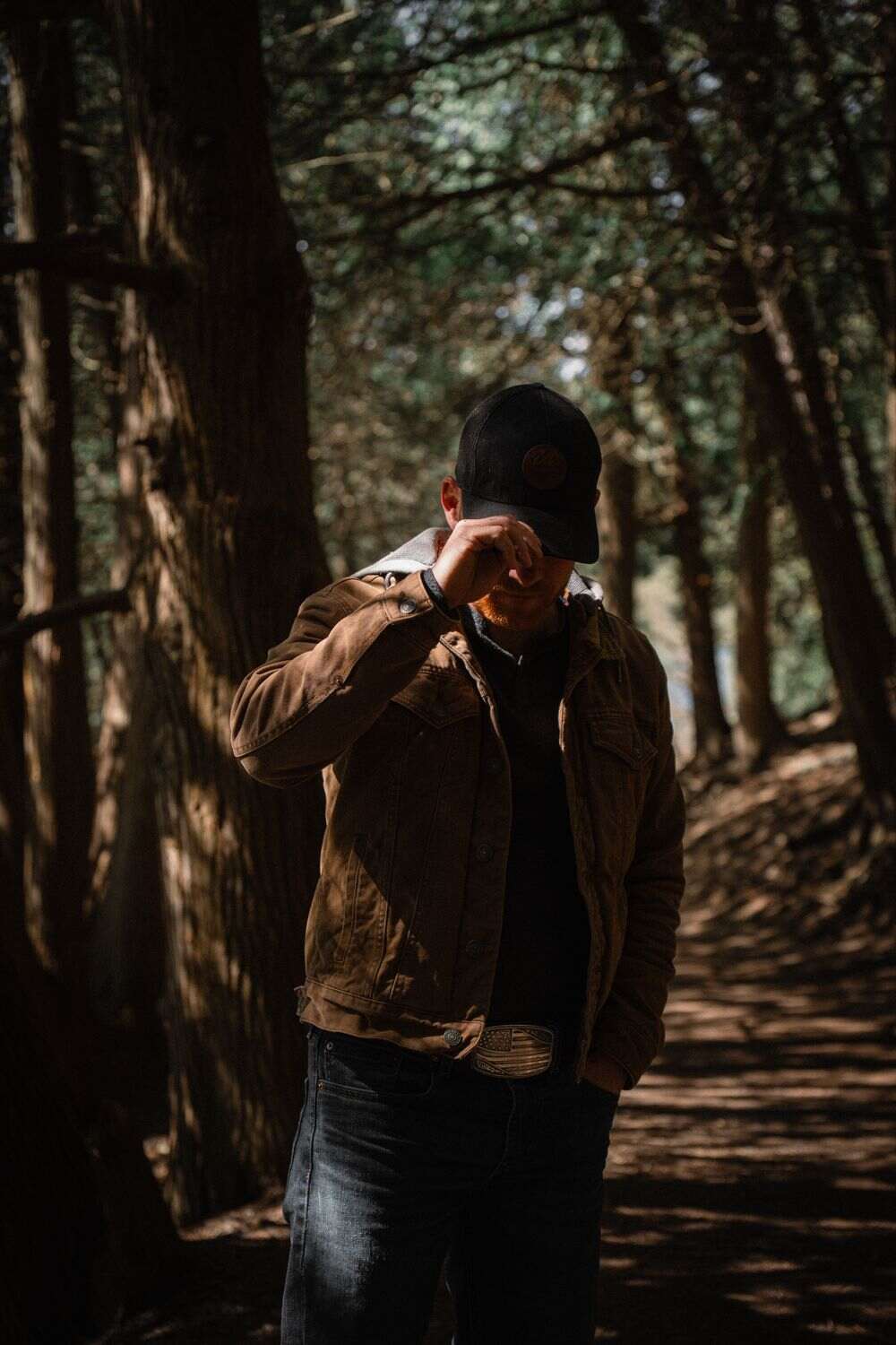 Steven Cali in a moody forest portrait, wearing a cap and jacket