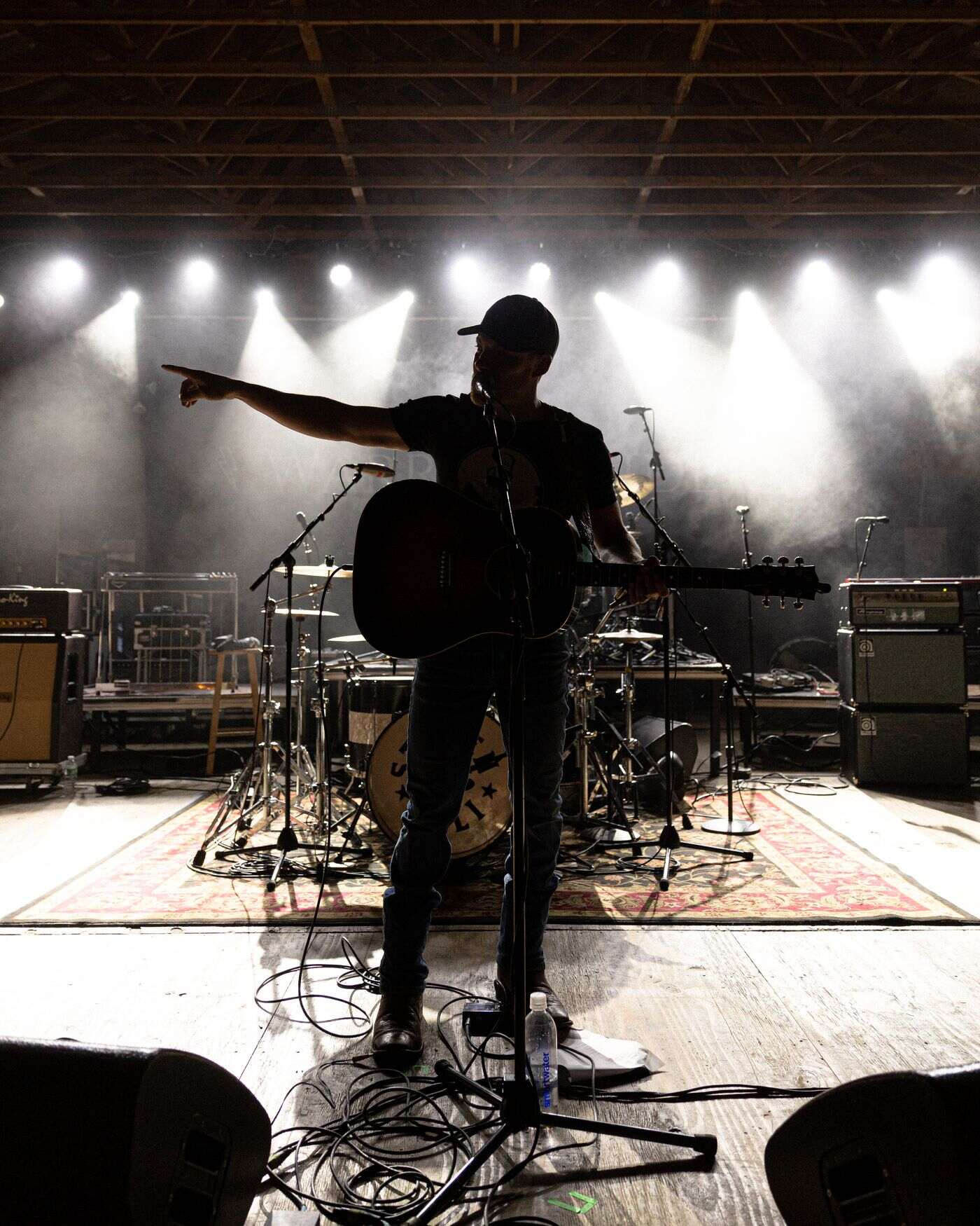 Steven Cali performing live on stage — a backlit silhouette pointing out over a hazy, warm-lit crowd