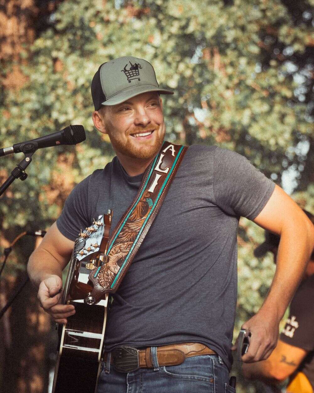 Steven Cali smiling warmly, guitar slung on a hand-tooled leather strap